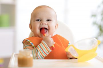 baby holding an orange spoon while eating